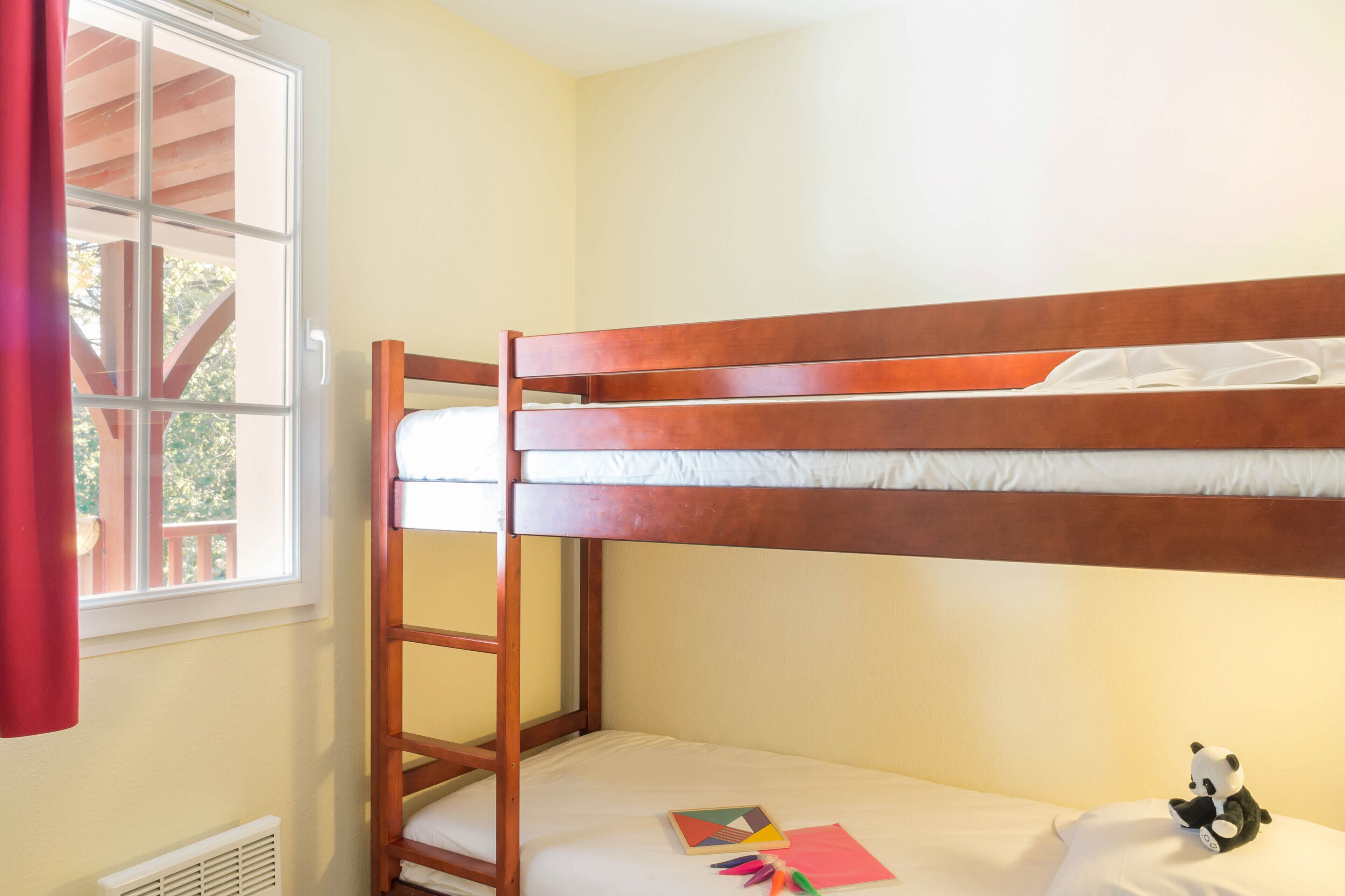 A bunk bed with a ladder, a window with a view of a deck, and a small panda toy on the lower bunk.