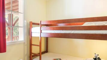 Una cama litera con una escalera, un ventanal con vistas a una terraza y un pequeño peluche de panda en la cama inferior.