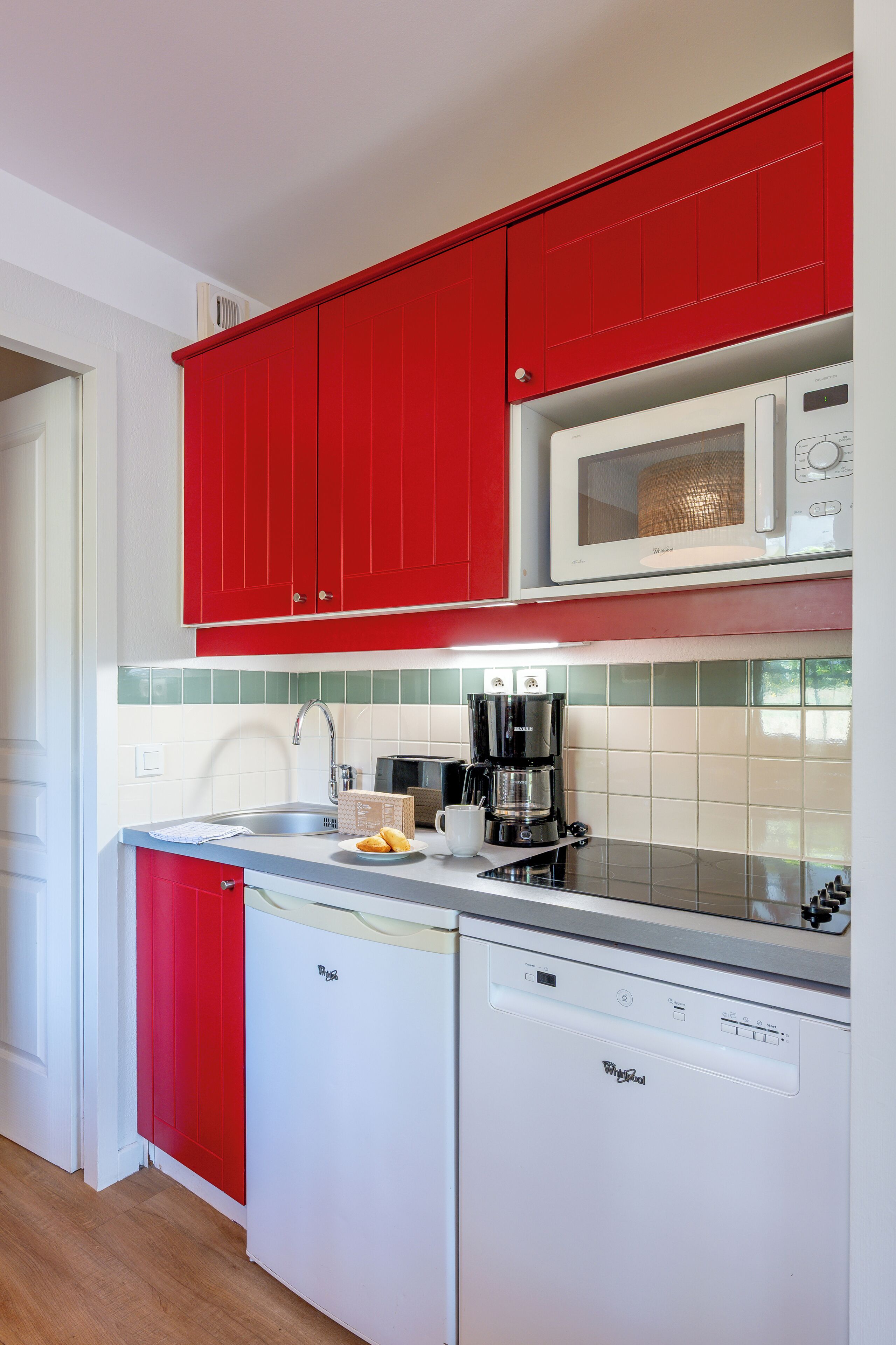 A compact kitchen with red cabinets, a microwave, a coffee maker, and a dishwasher.