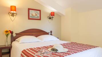 Una cama bien hecha con una colcha a rayas, una almohada blanca y una revista sobre la cama. Hay un florero con flores sobre una mesita de noche al lado de la cama.