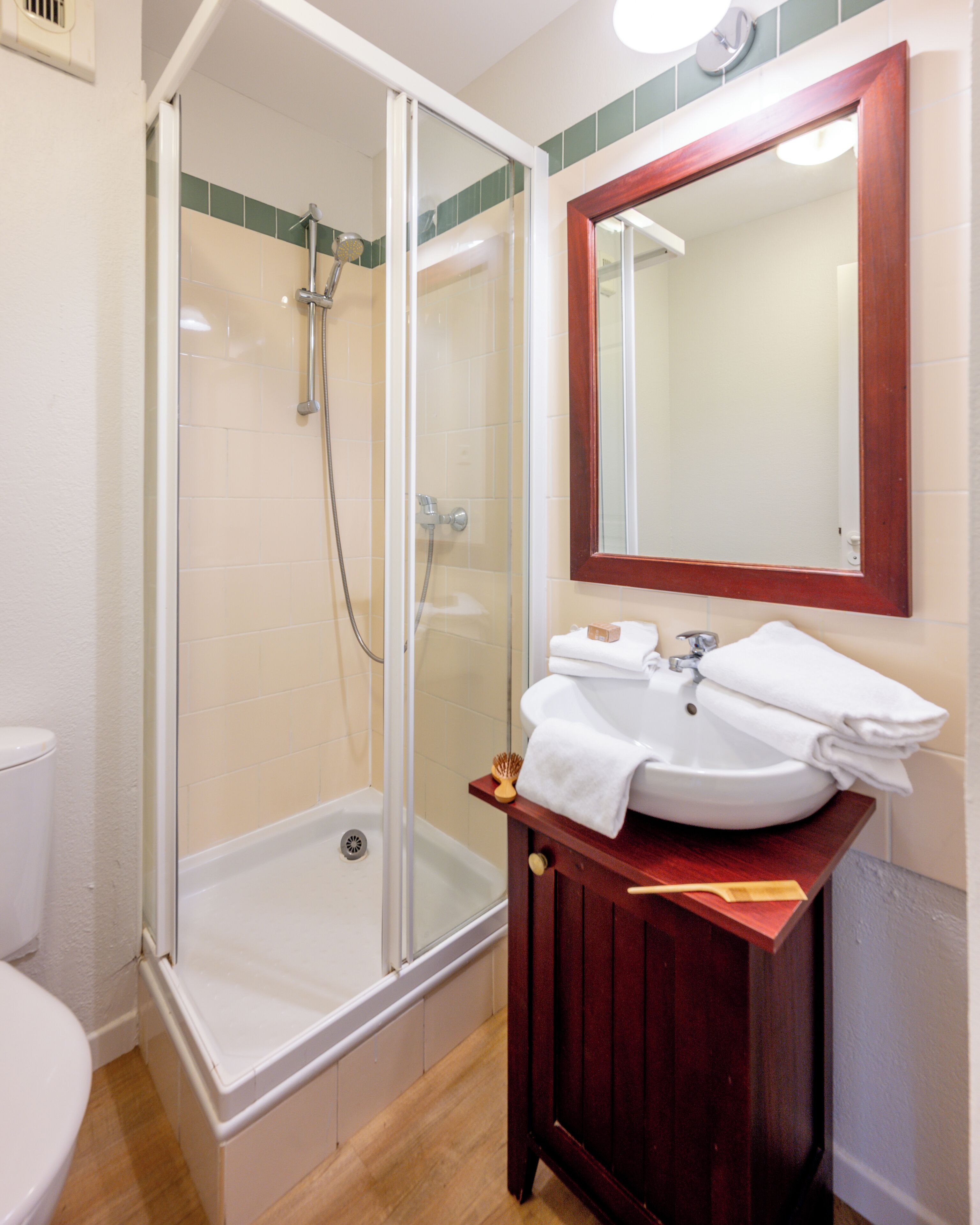 Un baño con ducha de vidrio, un lavabo blanco con tocador de madera y un espejo sobre el lavabo.