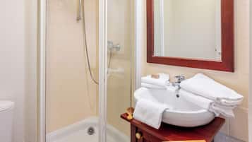 Un baño con ducha de vidrio, un lavabo blanco con tocador de madera y un espejo sobre el lavabo.