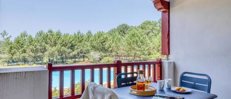 A balcony with a table set for two, overlooking a pool and a forested area.