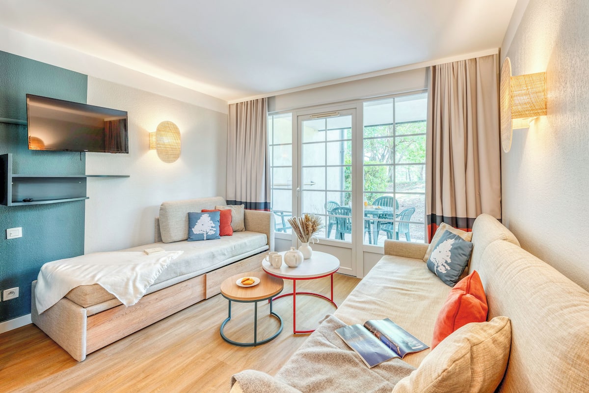 A modern living room with a sofa, two beds, a TV, and a window with curtains.