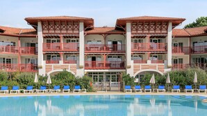 Ein Hotel mit Schwimmbad, mehreren Balkonen und blauen Liegestühlen.