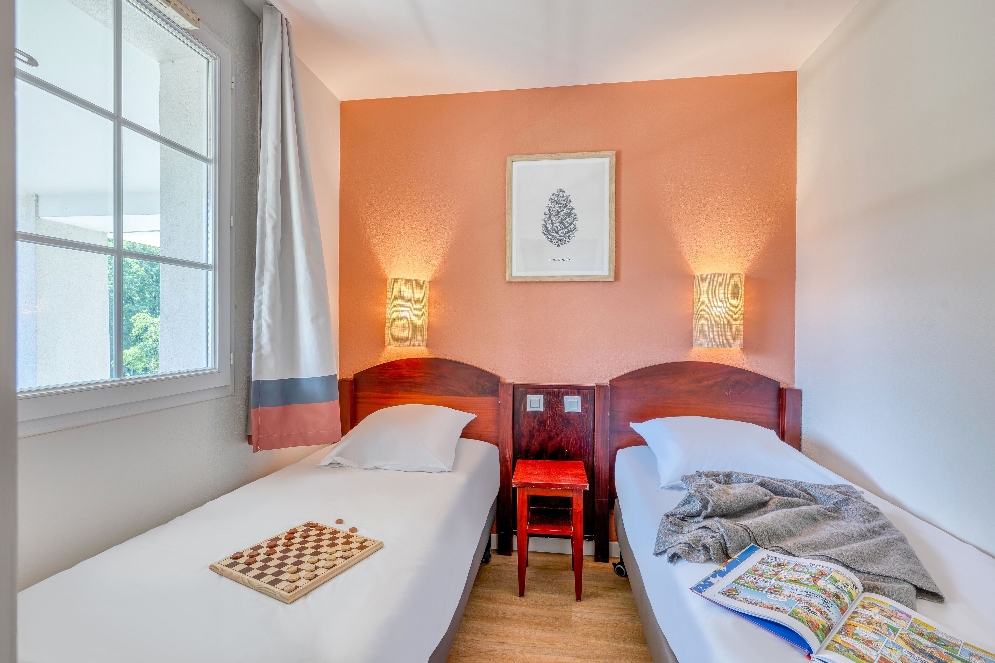 A hotel room with two beds, a small table, and a window with curtains.