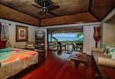 A room with a bed, a sofa, a dining table, and a view of the ocean.
