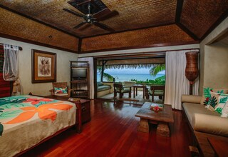 A room with a bed, a sofa, a dining table, and a view of the ocean.