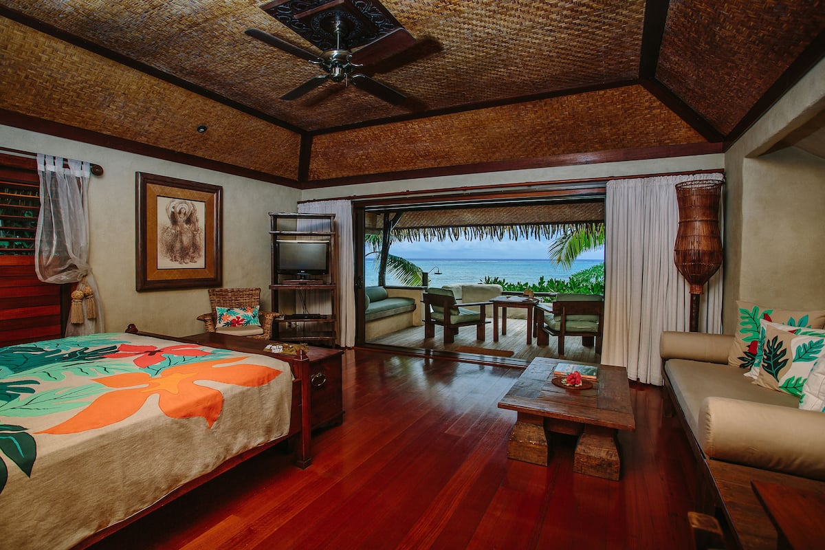 A room with a bed, a sofa, a dining table, and a view of the ocean.
