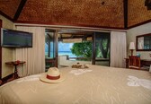 A hotel room with a large bed, a TV, a view of the ocean, and a balcony.