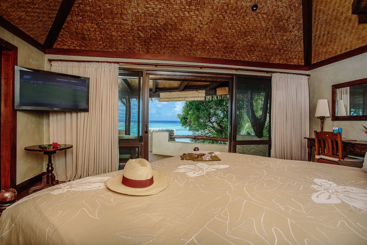 A hotel room with a large bed, a TV, a view of the ocean, and a balcony.