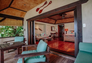 A spacious room with a wooden dining table, a sofa, and a large window overlooking greenery.