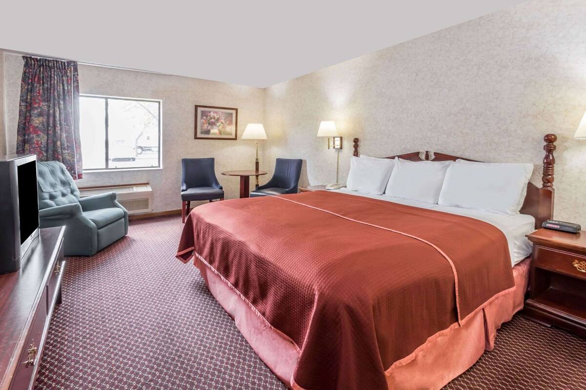 Hotelkamer met een groot bed, twee stoelen, een bureau, een televisie en een raam met gordijnen.