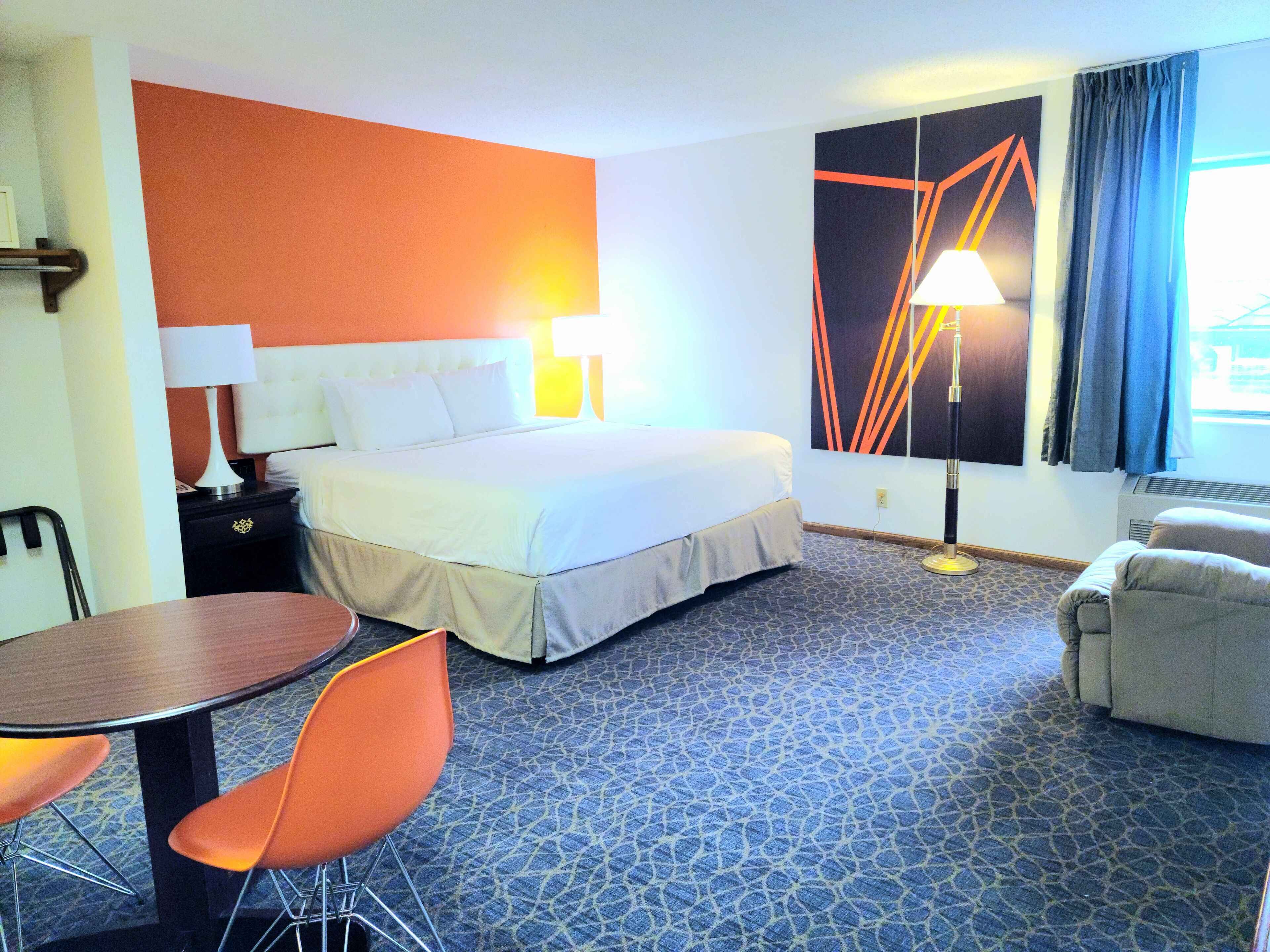 Habitació d'hotel amb un llit gran, una taula de treball amb una cadira, una làmpada i una finestra amb cortines.
