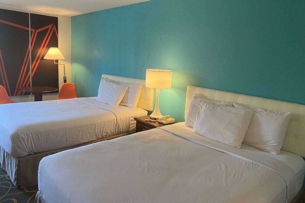 Een hotelkamer met twee bedden, een nachtkastje met een lamp en een muur met geometrische patronen.