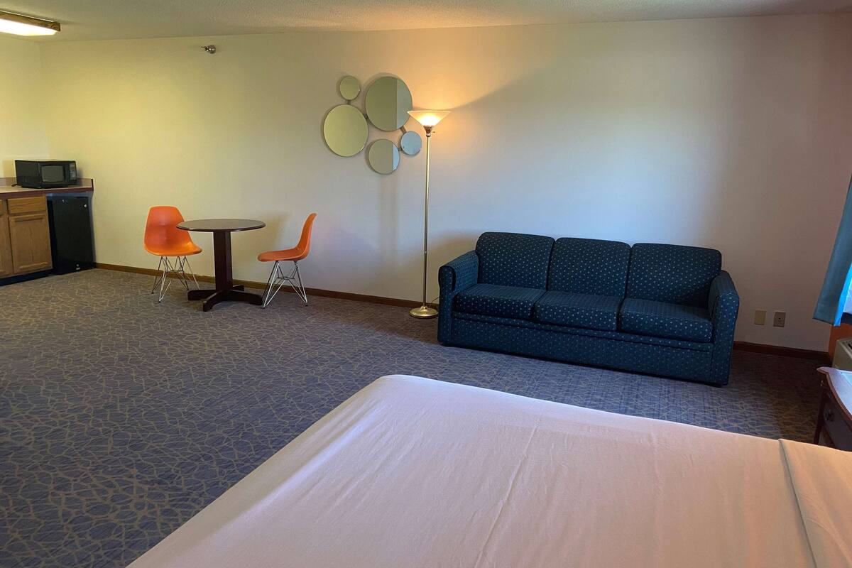 Een hotelkamer met een bed, een blauwe bank, twee oranje fauteuils, een tafeltje, een magnetron en een wandlamp.