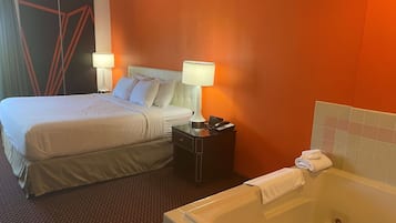 A hotel room with a large bed, two bedside tables with lamps, a small table with a phone and remote, and a bathtub with a towel.