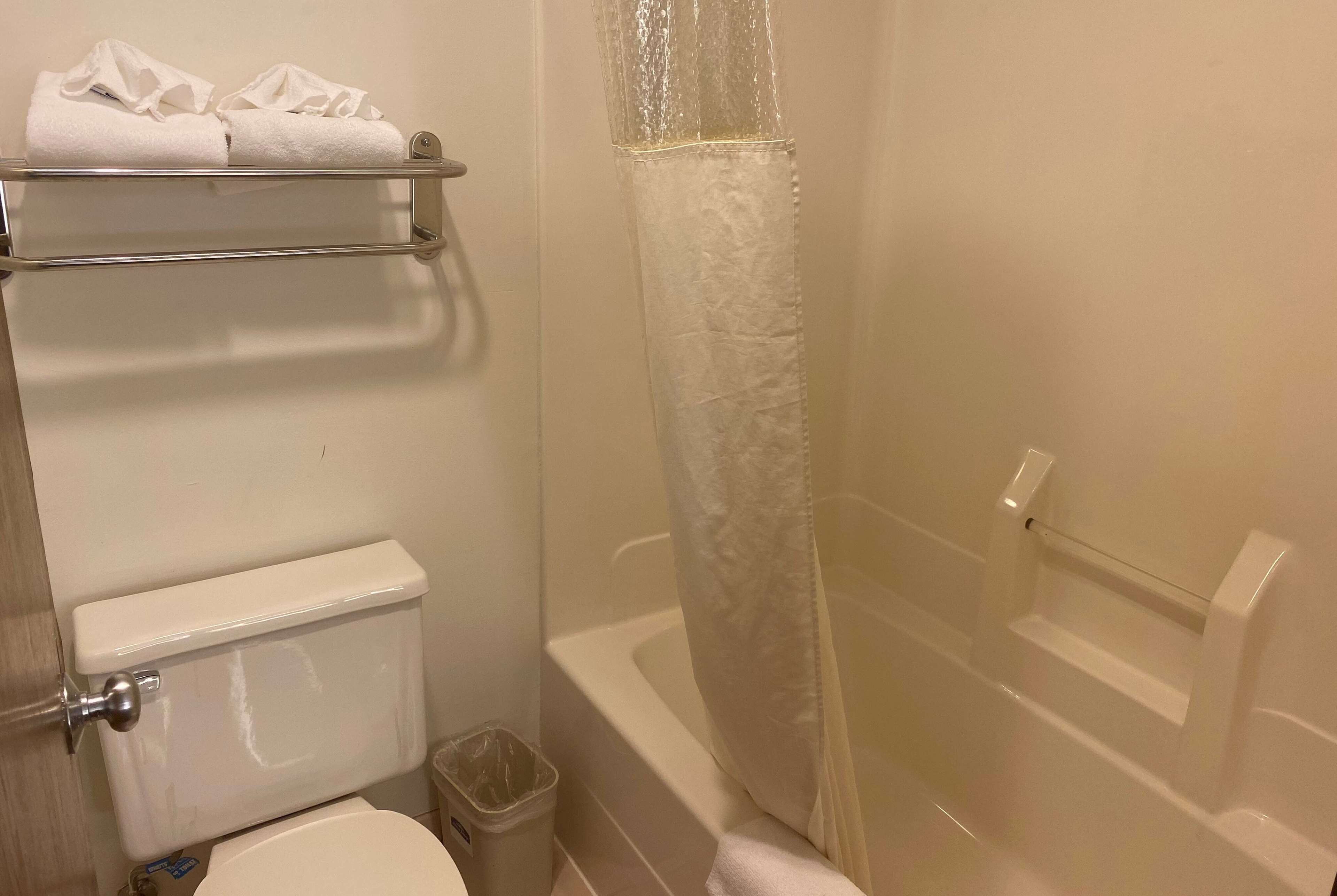 Un baño con inodoro, un cubo de basura, cortina de ducha y toallero con toallas.