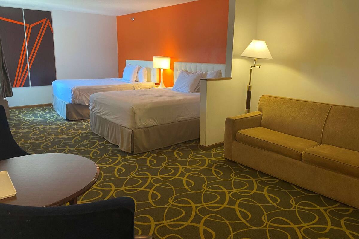 Een hotelkamer met twee bedden, een bank, een ronde tafel en een kamerbreed tapijt met een patroon.