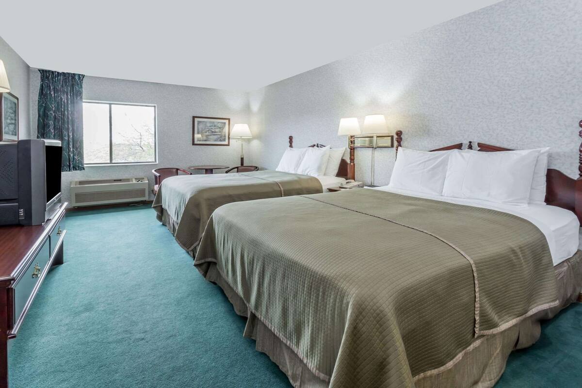 Een hotelkamer met twee bedden, een televisie, een bureau en een raam met gordijnen.
