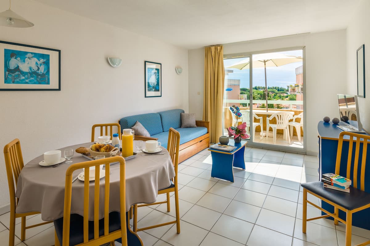 A dining area with a table set for breakfast, a sofa with cushions, and a view of the outdoors through a glass door.