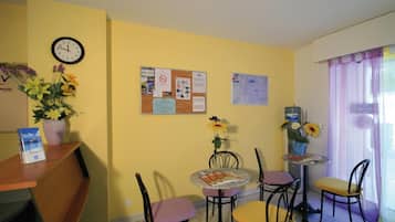 A dining area with a corkboard displaying notices, a clock, and a flower arrangement.