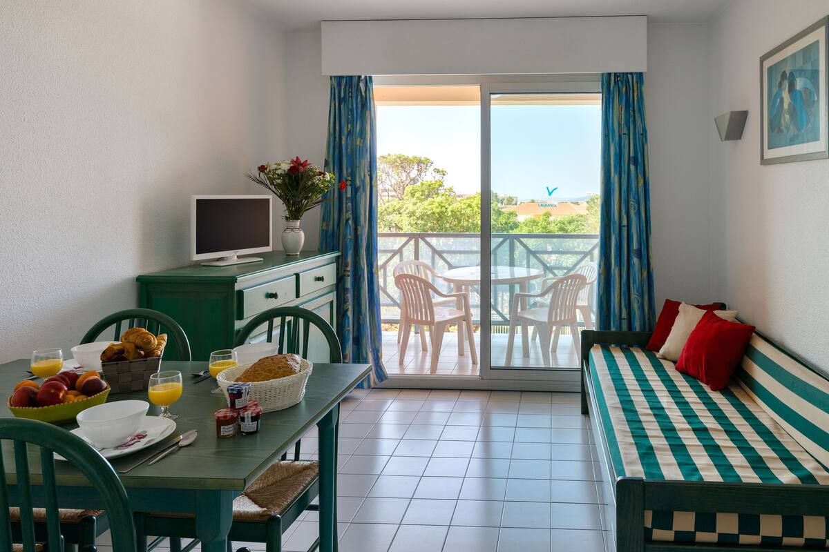 Een kamer met een eettafel gedekt voor het ontbijt, een bank en een balkon met stoelen.