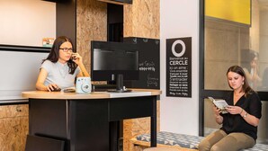 A modern interior with a reception desk, a computer, and a seating area with a patterned bench. - Aparthotel Adagio Access Paris Vanves Porte de Versailles (Vanves)