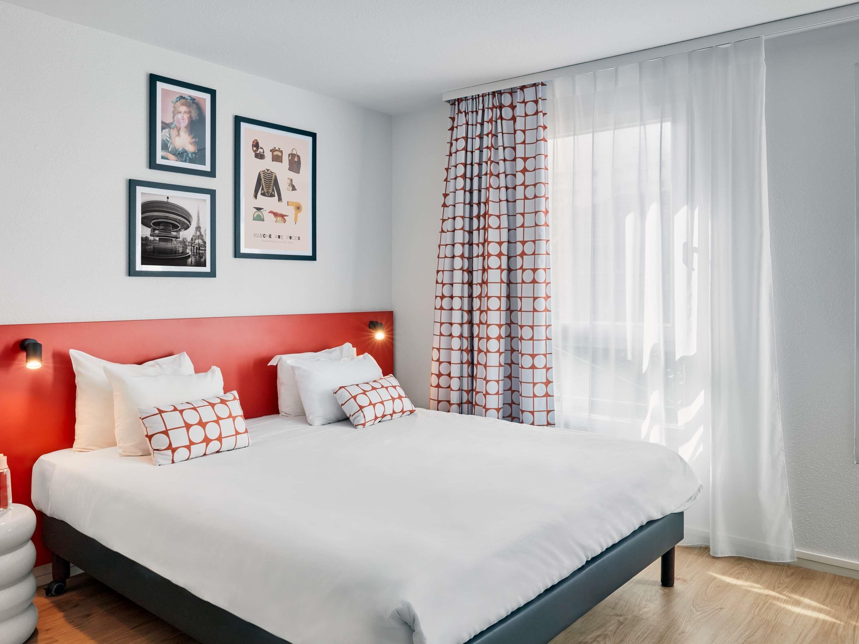 A modern hotel room with a large bed, a red headboard, and three framed pictures on the wall.
