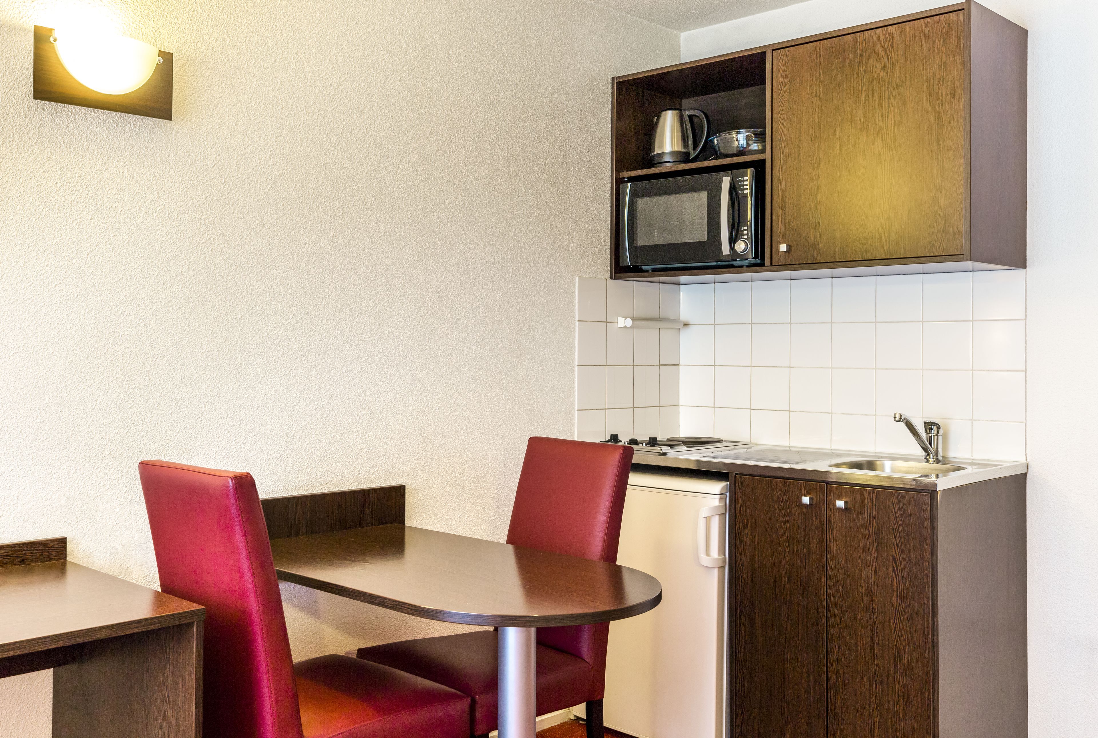 Une cuisine compacte équipée d’un four à micro-ondes, d’un évier et d’un petit réfrigérateur. On y trouve également une table à manger avec deux chaises.
