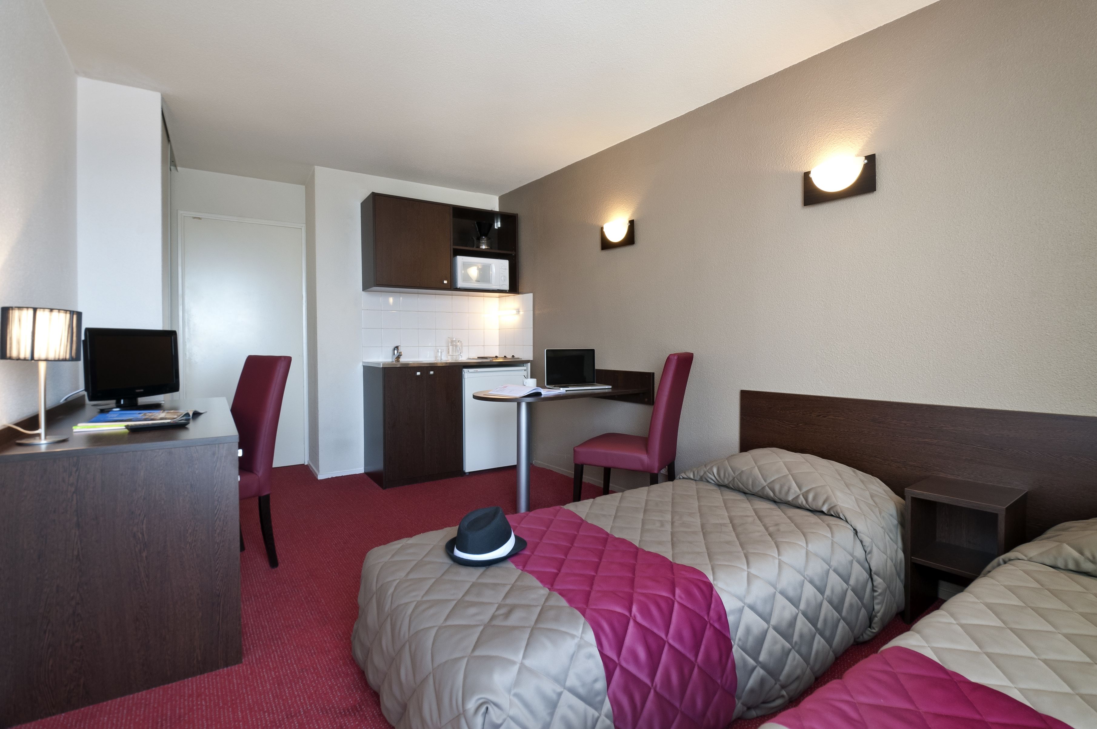 Ein Hotelzimmer mit Bett, Schreibtisch, Stuhl und Küchenzeile.