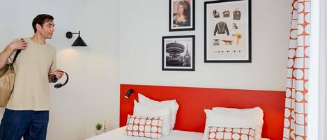A hotel room with a bed, pillows, a lamp, and a wall with framed pictures.