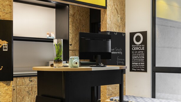 A modern kitchen area with a bar stool, a coffee machine, and a sign on the wall. - Aparthotel Adagio Access Paris Vanves Porte de Versailles (Vanves)