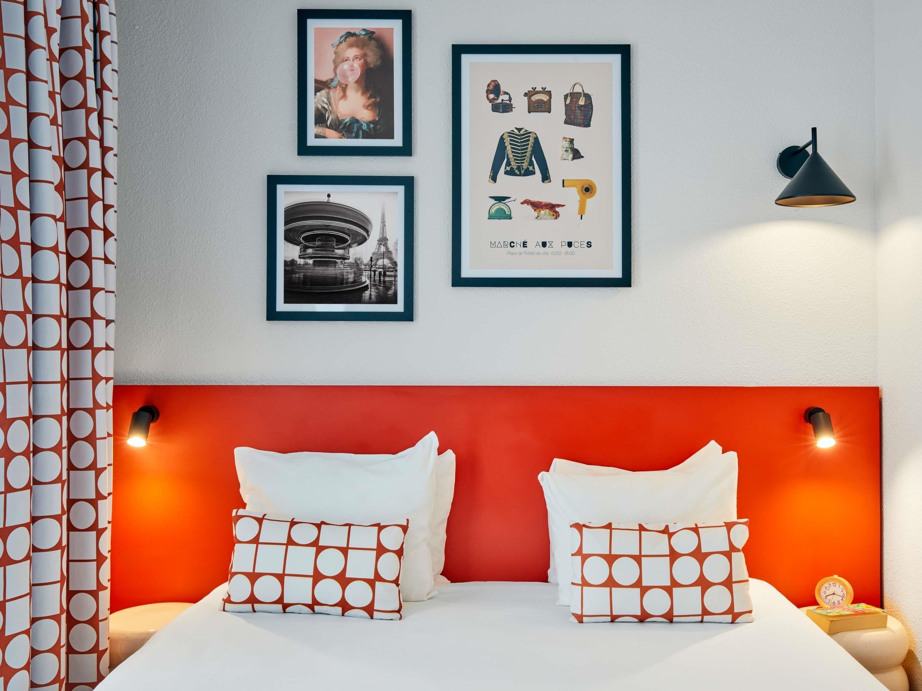 Habitación de hotel con cama, almohadas, un cuadro con vista de la ciudad, un cuadro de una mujer y un cuadro de equipaje.