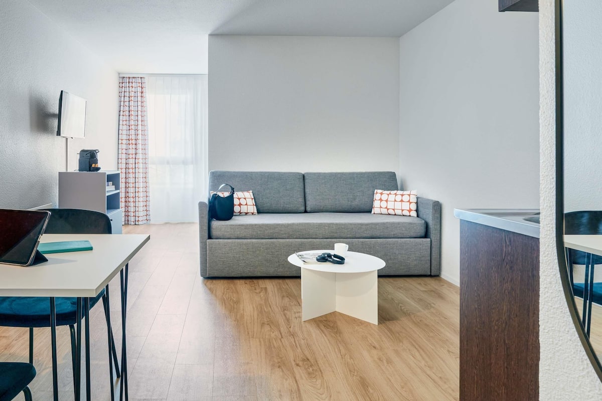 Un salon moderne avec un canapé gris, une table basse, un bureau avec un ordinateur portable et un téléviseur fixé au mur.