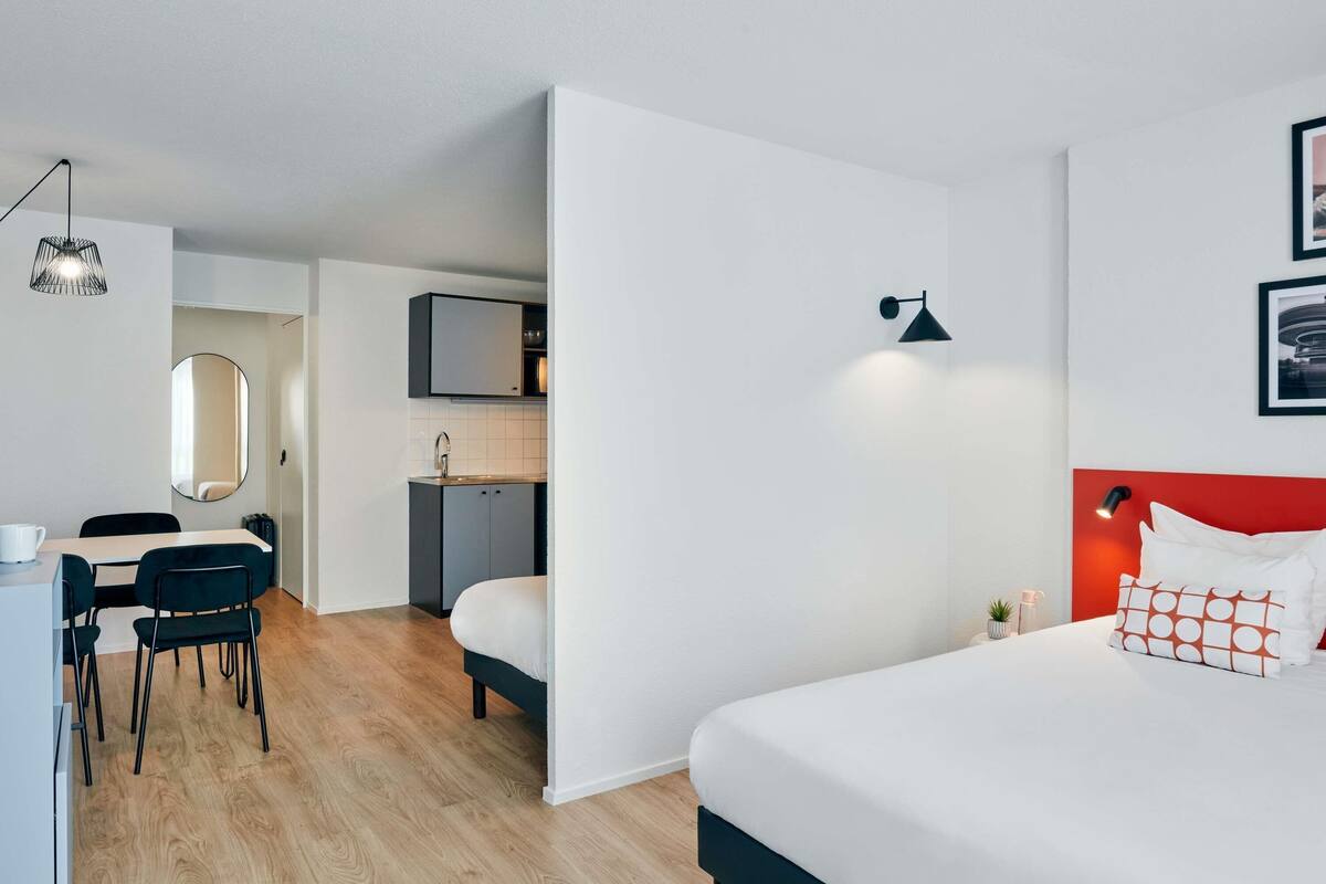 Une chambre d’hôtel moderne équipée d’un lit, d’un bureau avec des chaises, d’une kitchenette et d’une salle de bain.