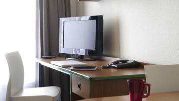 A hotel room with a wooden desk, a white chair, a red mug, and a book.