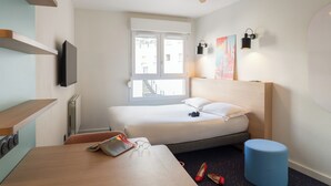 A hotel room with a bed, a desk, a chair, a ceiling fan, a window, and a wall-mounted TV. - The Originals Résidence, Appart’Hôtel les Lauréades, Clermont-Ferrand (Clermont-Ferrand)