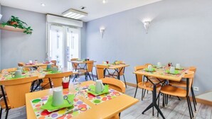 A brightly lit dining area with multiple tables and chairs, equipped with table settings and a potted plant. - The Originals Résidence, Appart’Hôtel les Lauréades, Clermont-Ferrand (Clermont-Ferrand)