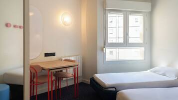 Une chambre avec deux lits, un bureau avec des chaises, une lampe fixée au mur et une fenêtre.