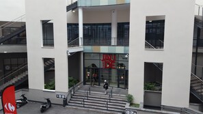 Ein mehrstöckiges Gebäude mit einem zentralen Eingang, Glasüren und einem Schild mit der Aufschrift 'JAY DE'.