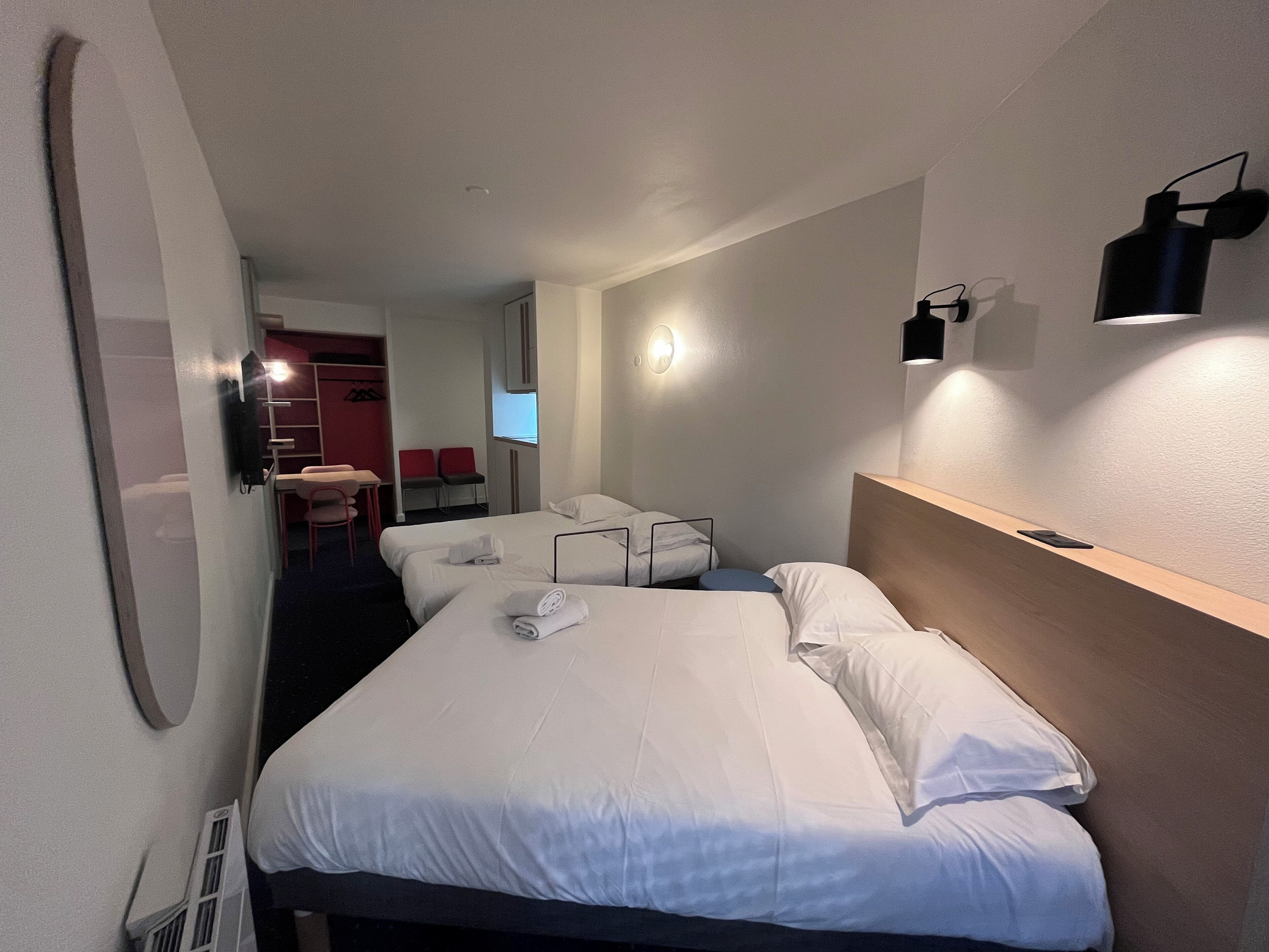 A hotel room with two beds, a desk, a chair, and a TV.