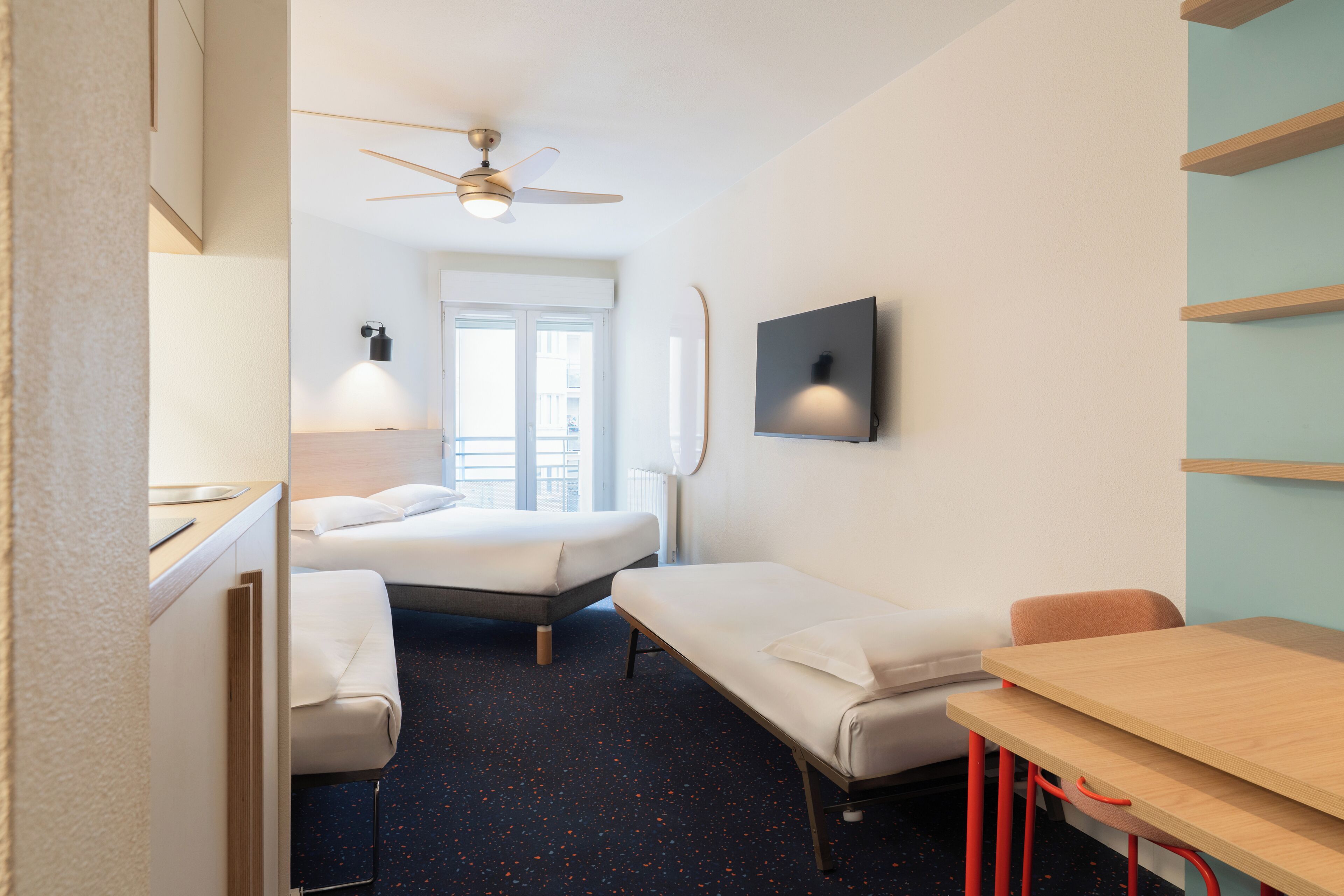 Habitación de hotel con cama, escritorio, silla, ventilador de techo, televisor y ventana.