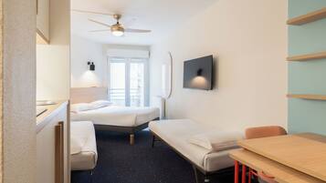 Habitación de hotel con cama, escritorio, silla, ventilador de techo, televisor y ventana.