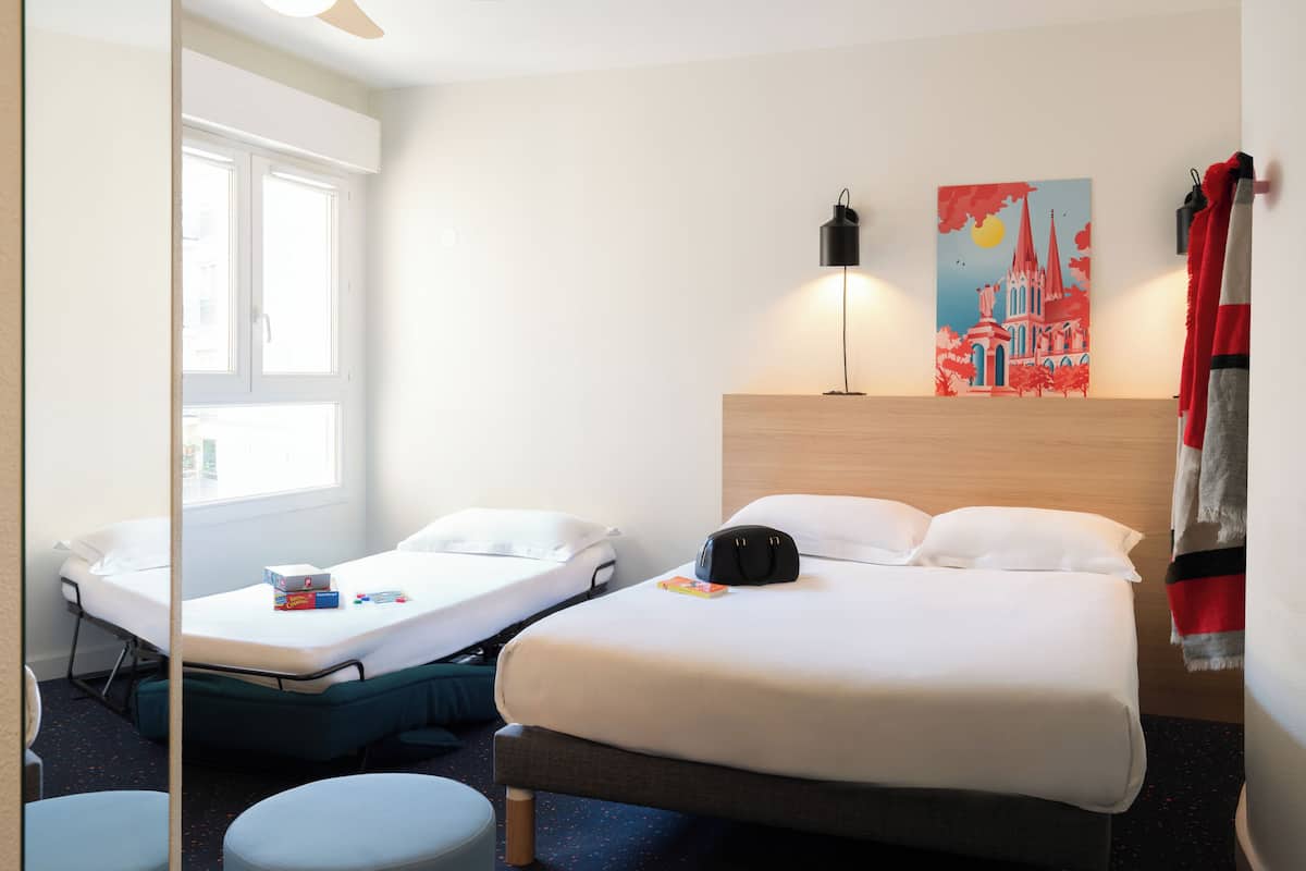 Ein Hotelzimmer mit einem Bett, einem zusätzlichen Bett, einem Schreibtisch, einem Stuhl, einer Lampe und einem Bild an der Wand.