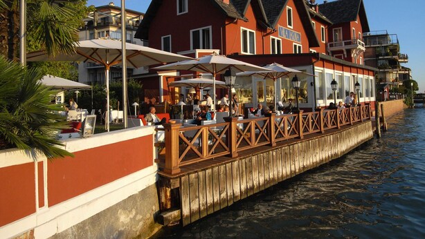 Een restaurant aan het water met terras, een houten dek en een gebouw met balkons in het rood.