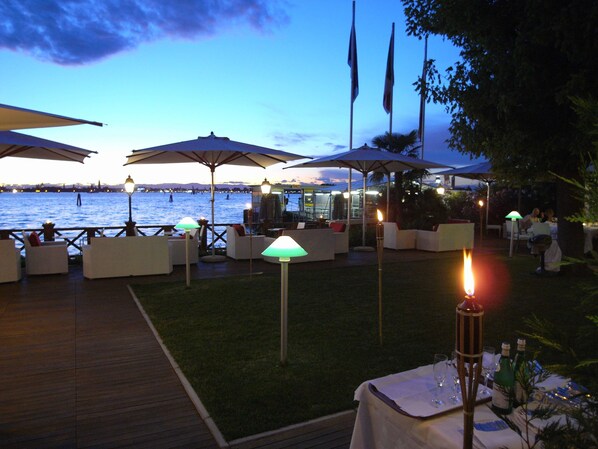 An outdoor dining area with tables and chairs, umbrellas, and a view of the water.