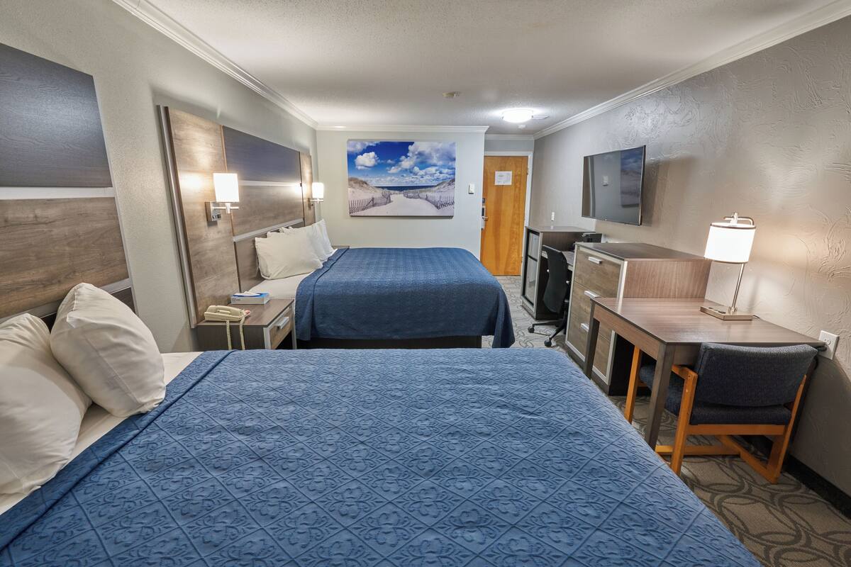 A hotel room with two beds, a desk, a chair, a TV, and a painting on the wall.