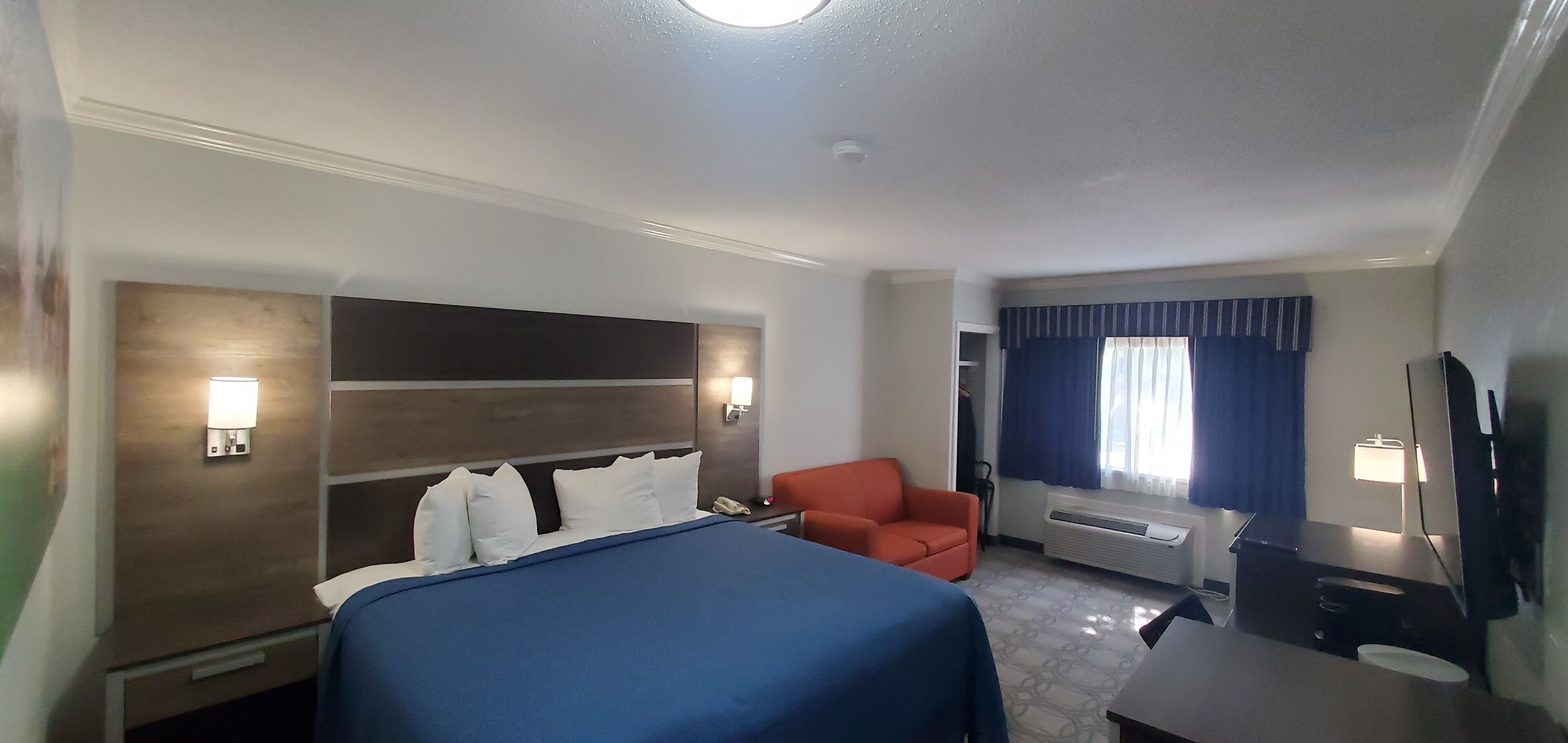 A hotel room with a bed, a desk, a chair, a TV, and a window with curtains.