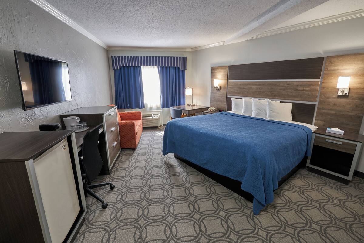 A hotel room with a bed, desk, chair, and a TV.